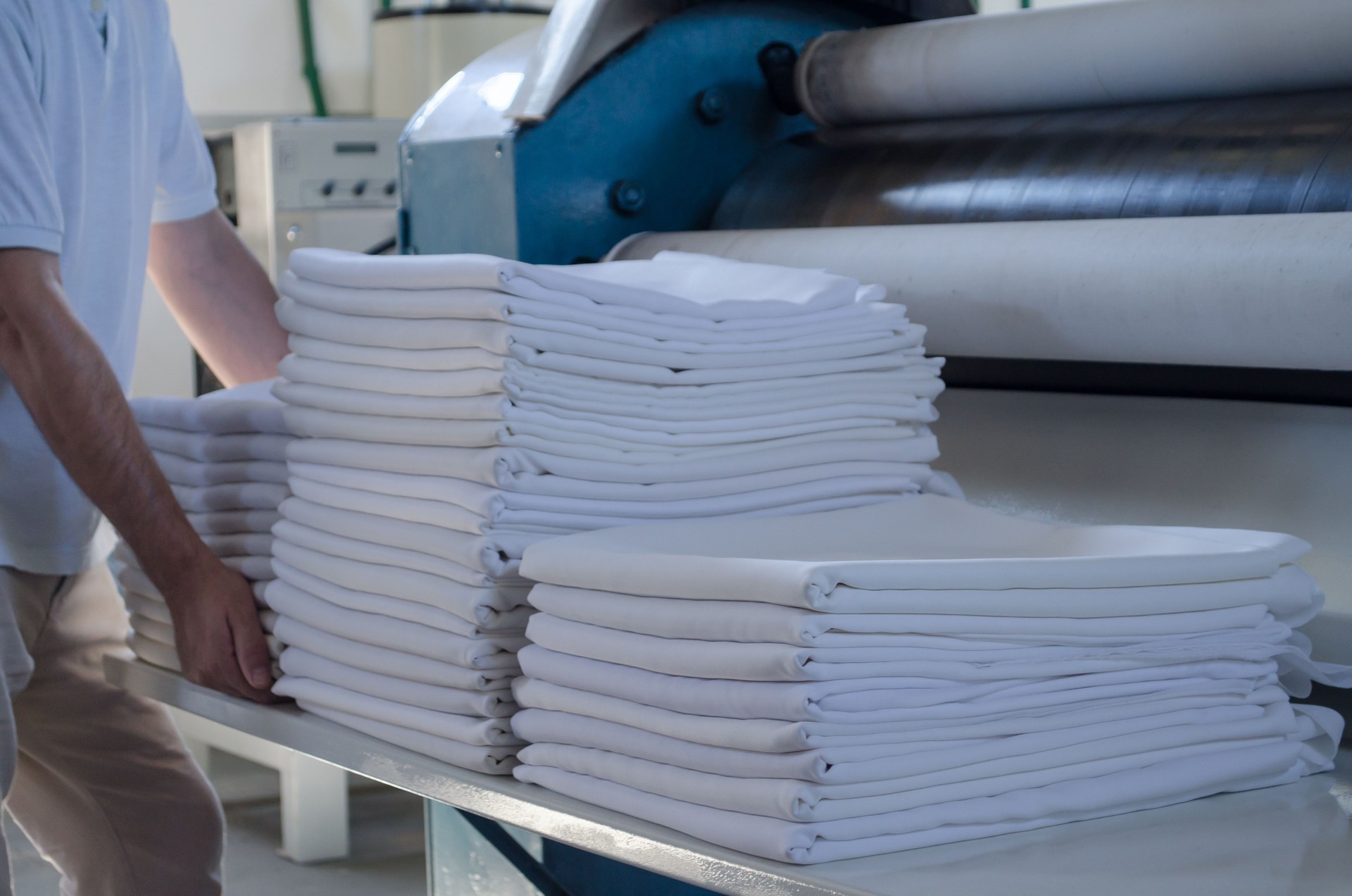 Unrecognizable man stacking freshly ironed sheets or fabrics in an industrial laundry. Cleaning and ironing service for hotels, clinics and companies.